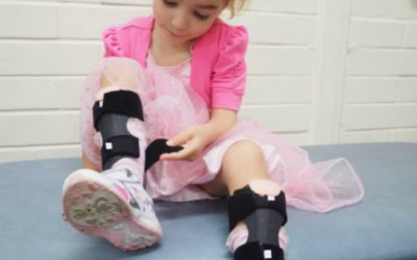 Young girl in pink dress, sitting down and putting on her ankle foot orthotic