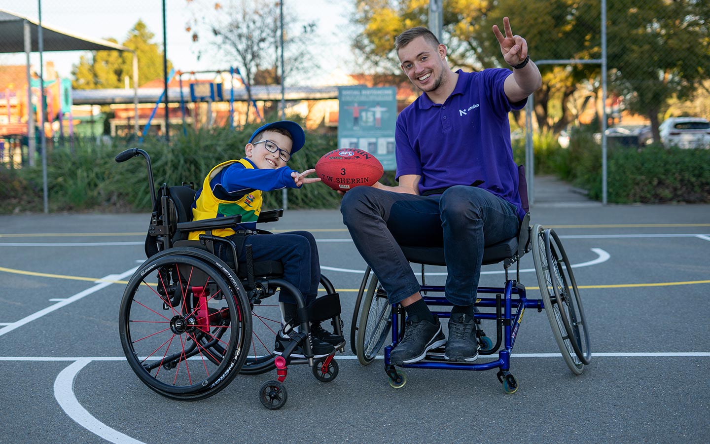 Young boy in a wheelchair and man in a wheelchair holding a football